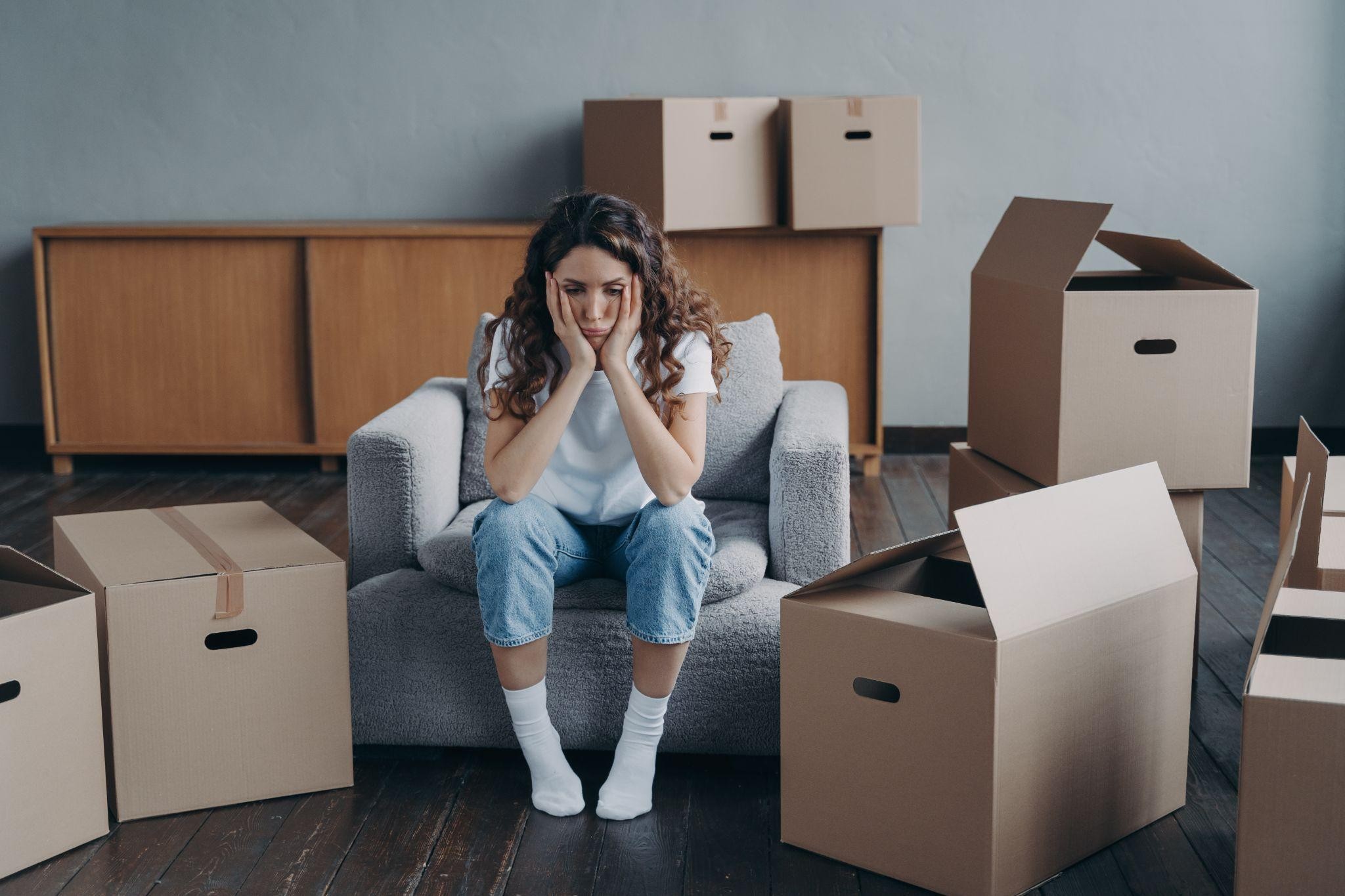 Go with Option 1: "A stressed female tenant sitting in an armchair, holding her face in her hands, surrounded by cardboard moving boxes in a sparse room.